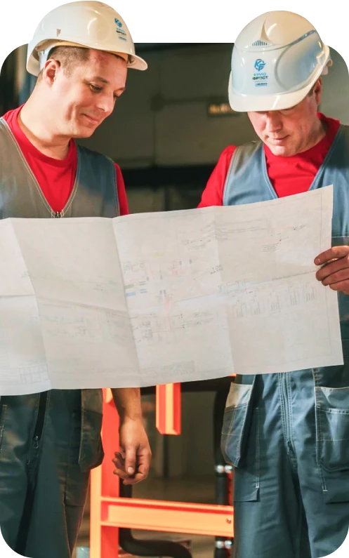 Двое рабочих в белых касках смотрят на чертеж